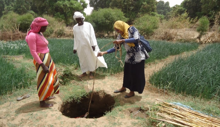 Women using a small container to withdraw water from a traditional well